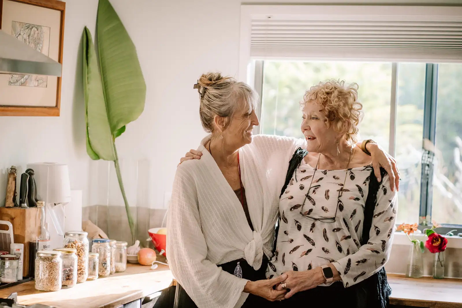 Two people talking and smiling together in a sunlit kitchen