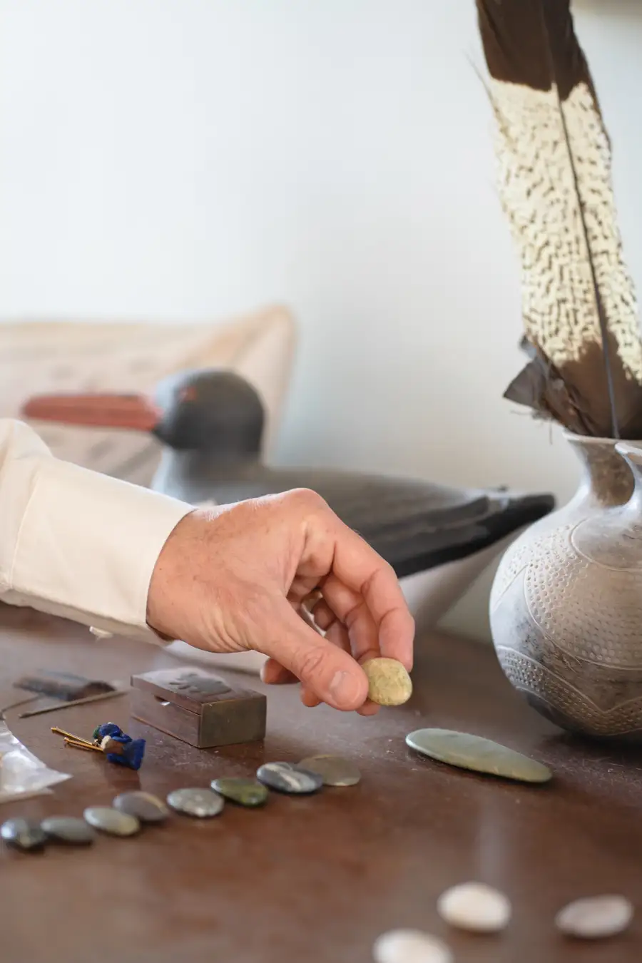 Close detail of hands arranging smooth stones beside carved objects on a wooden table