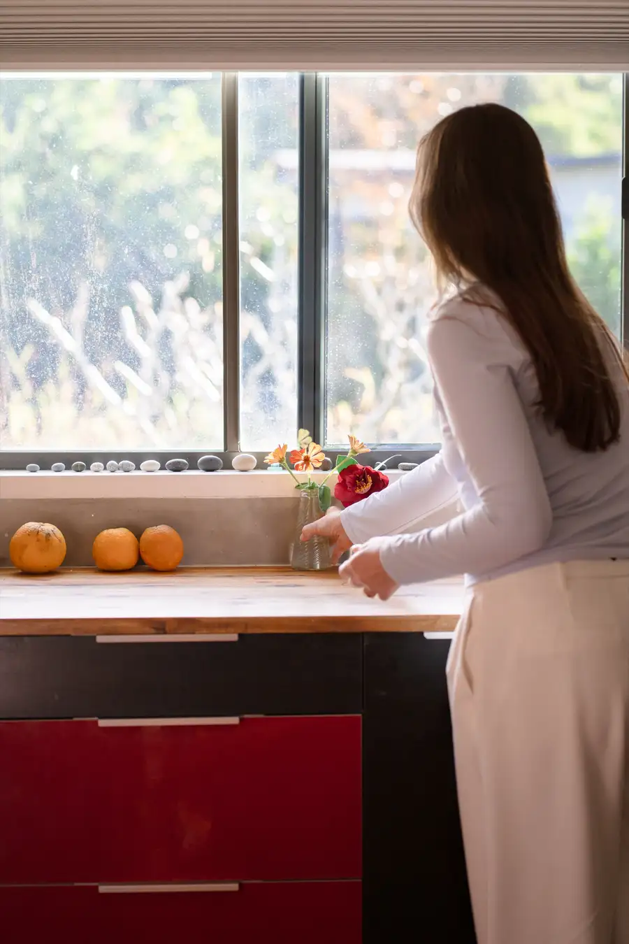 A clinician arranging fresh flowers by a sunlit window in a warm, homely clinic kitchen