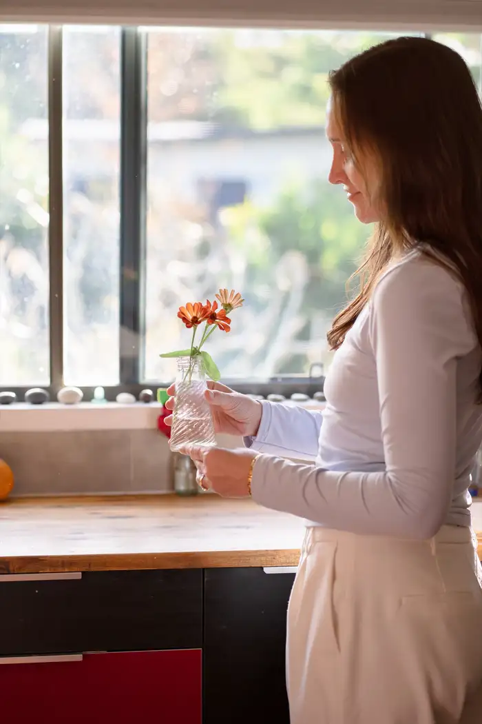 A clinician holding a small vase of flowers by a sunlit window in a calm clinic space