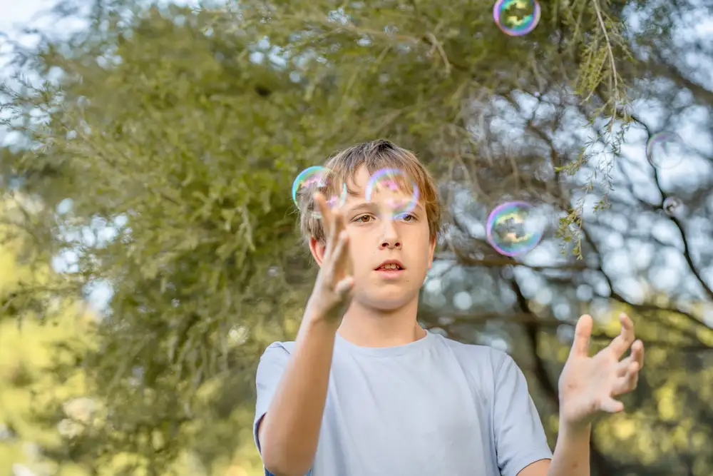 A teenager outdoors reaching for bubbles under a tree