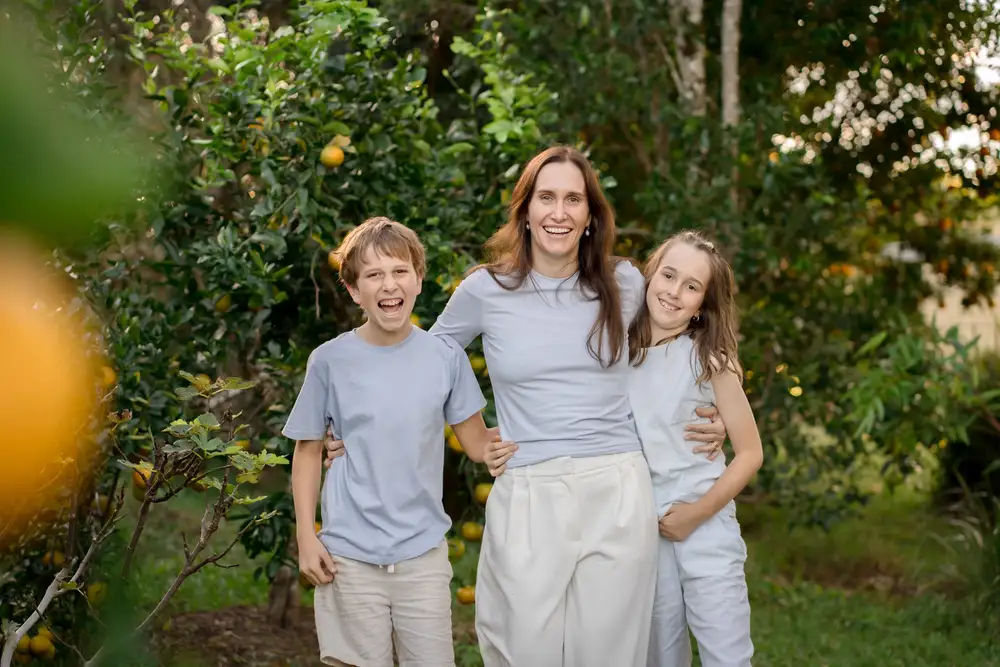 A family of three walking outdoors in an orchard, smiling
