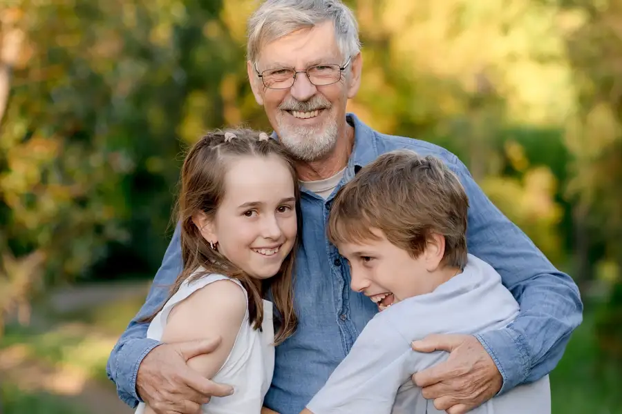 A grandfather sharing a warm hug with two grandchildren outdoors in golden afternoon light