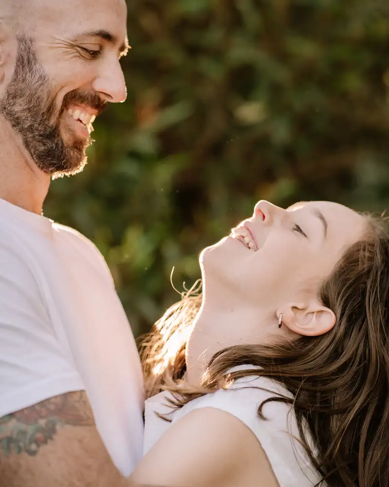 An adult and a young person laughing together outdoors at golden hour
