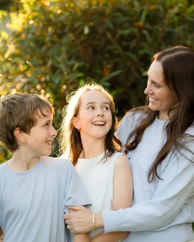 A parent and two children smiling together outdoors in golden afternoon light