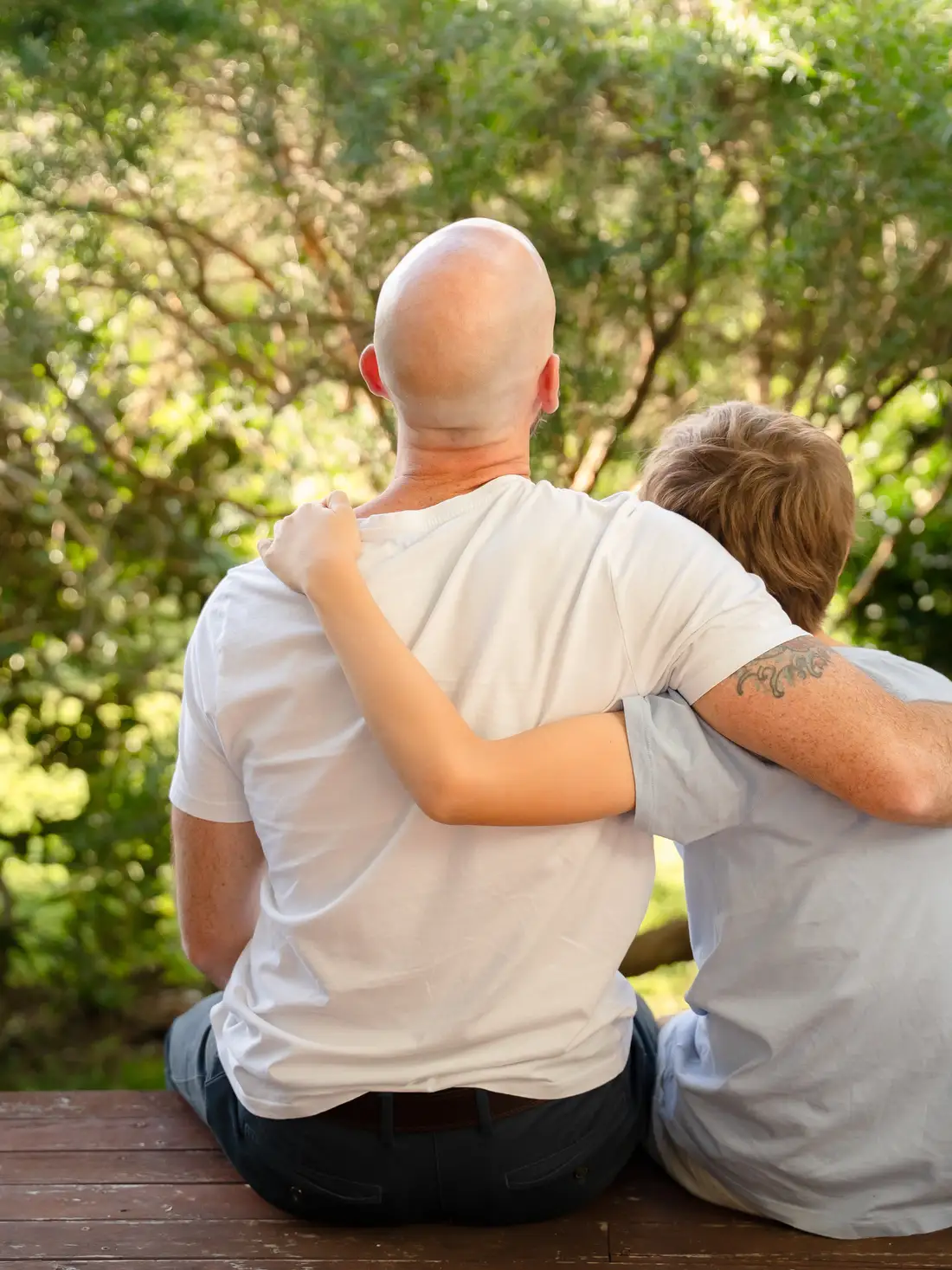 An adult and a child sitting close together outdoors among the trees