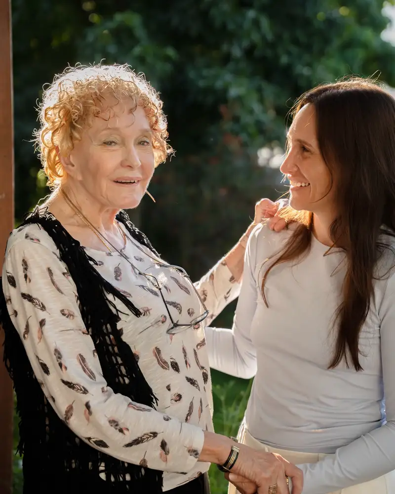 An older woman and a younger woman smiling warmly together outdoors