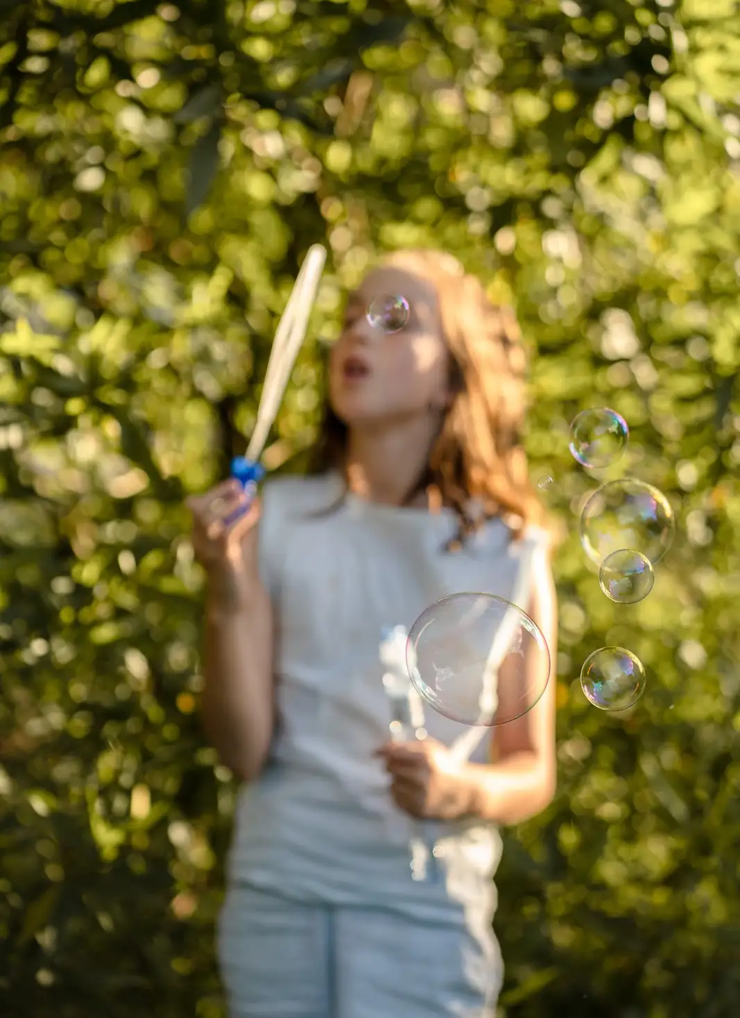 A child blowing bubbles outdoors in golden afternoon light
