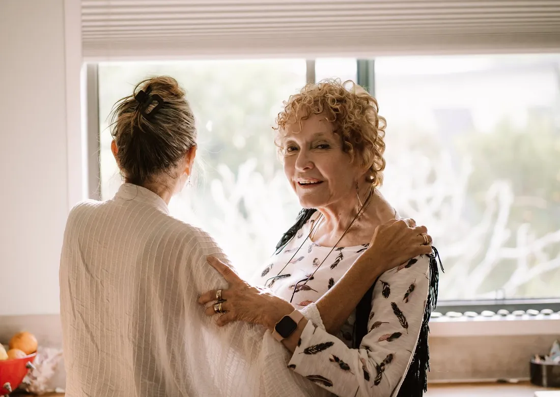 A support worker sitting with an older woman in a sunlit lounge room