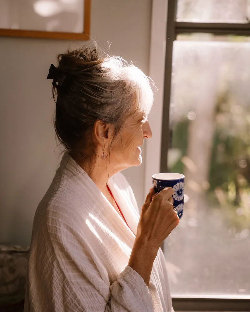 An older woman relaxing with a warm drink by a sunlit window